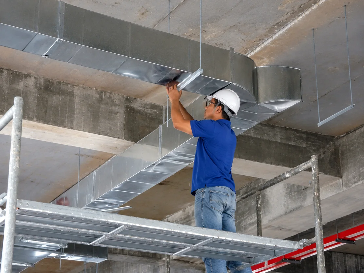 Técnico instalando rede de dutos galvanizados de climatização em obra industrial