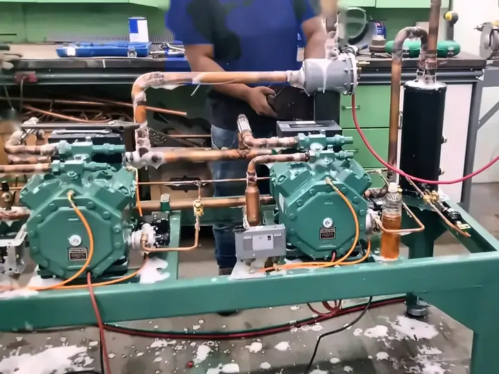 Técnico montando um rack de compressores na oficina, com teste de vazamento com espuma e nitrogênio