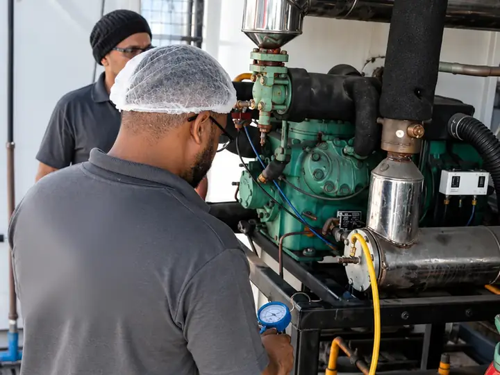 Técnicos da Refrigeração Schmökel medindo a pressão de um compressor industrial com manômetro